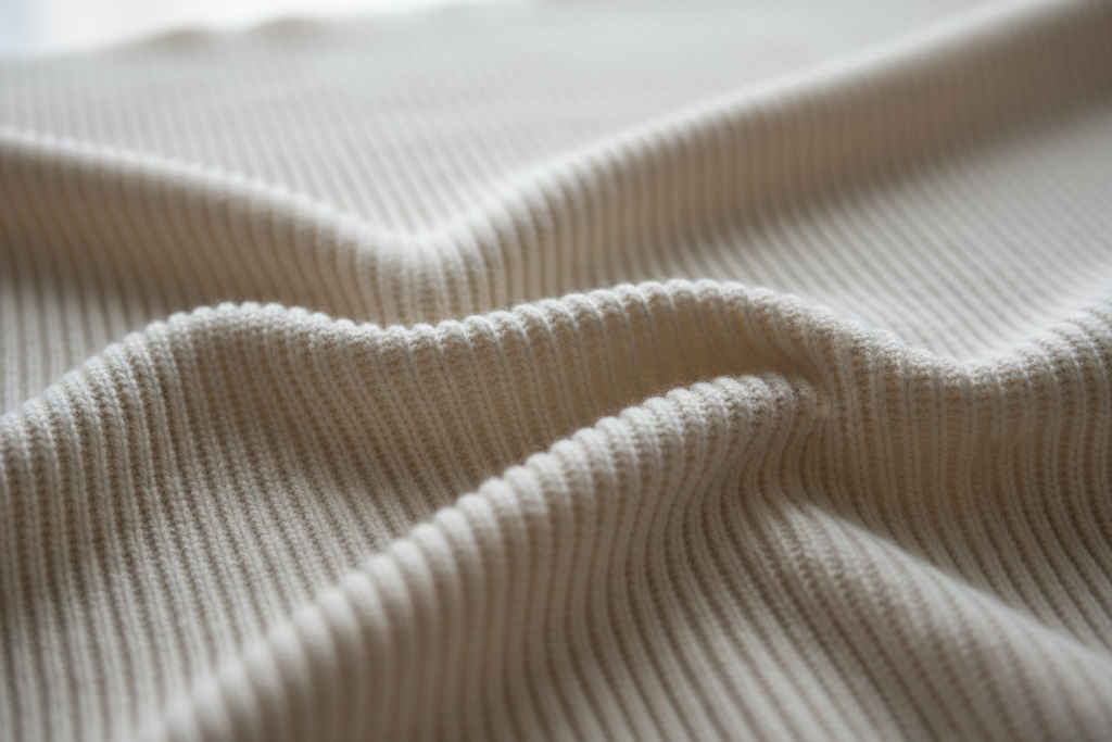 Our Organic Cotton Rib is a GOTS-Certified essential knit fabric defined by its vertical, corded pattern, created by alternating knit and purl stitches (typically 1x1 or 2x2 rib). This structure makes the fabric inherently elastic, incredibly durable, and capable of excellent shape recovery without relying heavily on synthetic elastomers like spandex.
